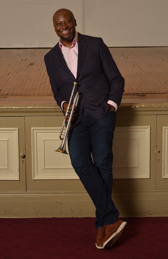 Sean Jones holding his trumpet and leaning against a stage