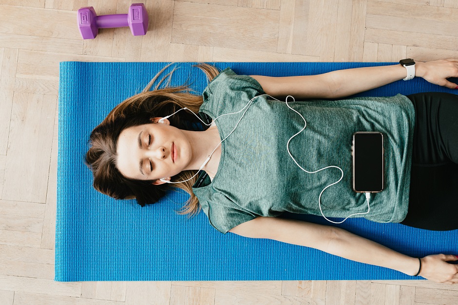 Female on yoga mat with eyes closed and wearing ear buds