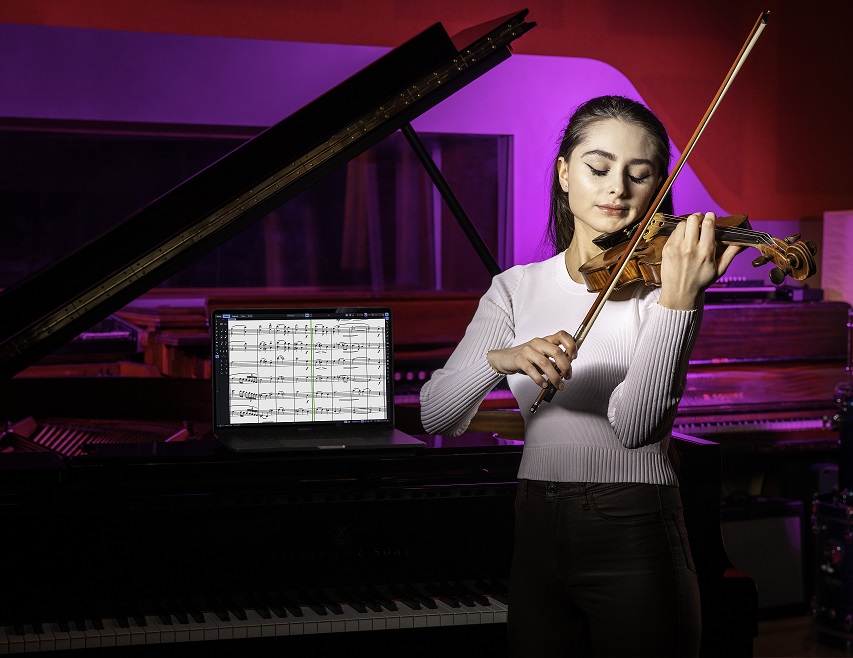 Violinist standing next to piano with Dorico notation software showing on a laptop screen