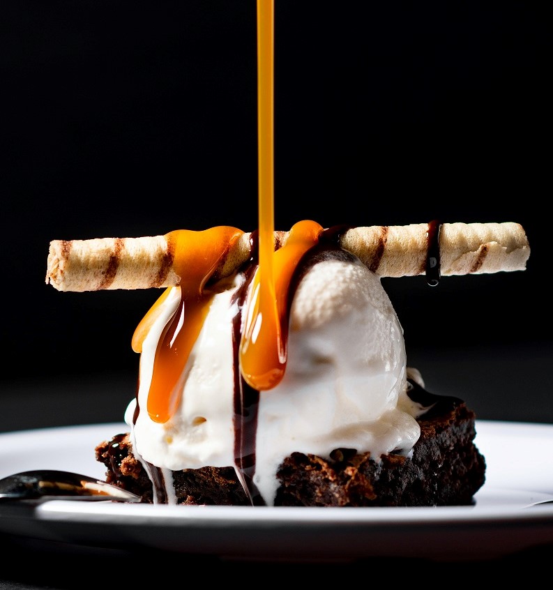 decadent dessert -- brownie topped by ice cream and caramel drizzle 