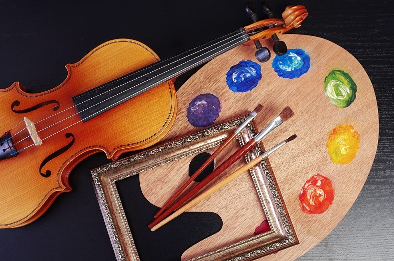 depicting the arts -- a violin, a palette, an empty frame and some paint brushes