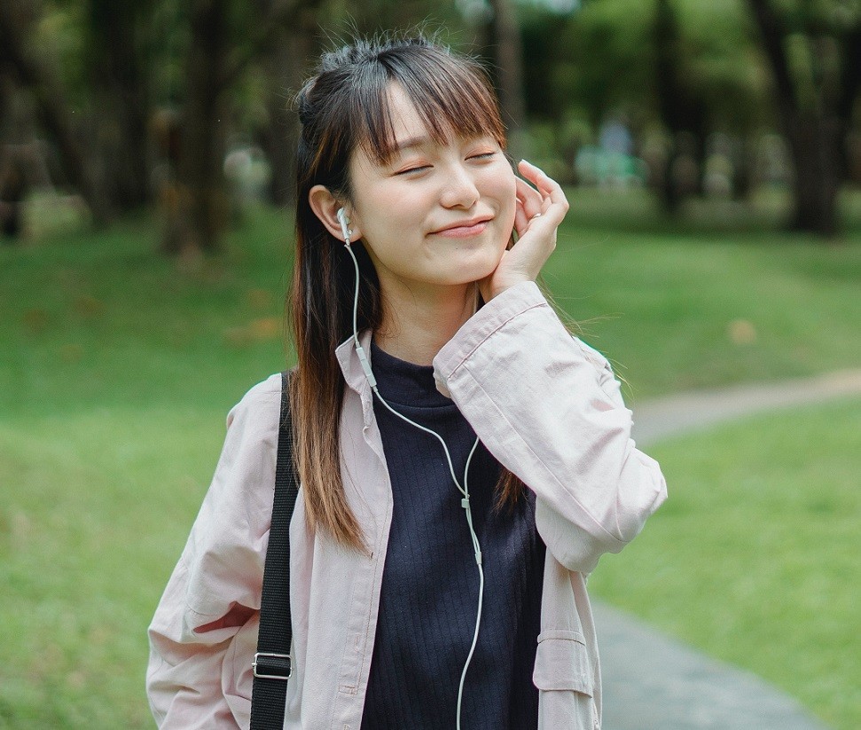 female Asian student walking while listening to music on earphones