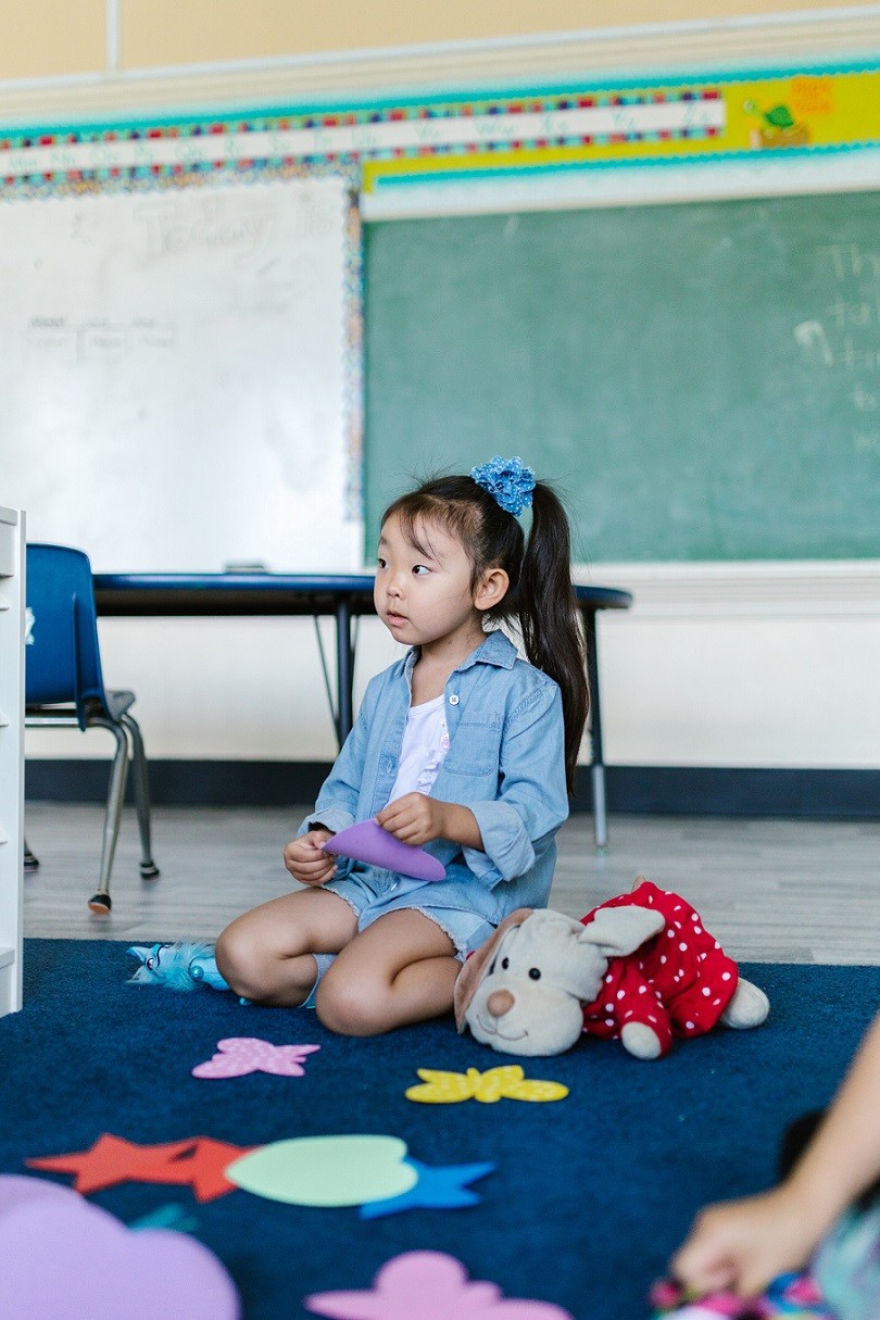 female Asian elementary student sitting on classroom rug 