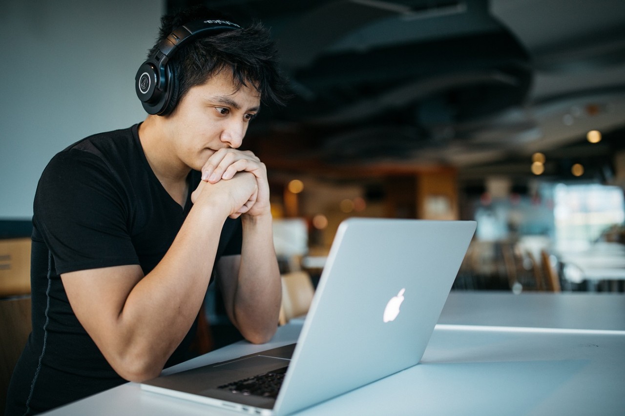man sitting in a coffee shop in front of laptop with headphones on 