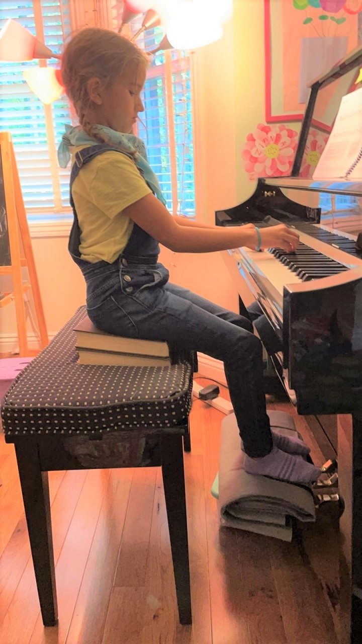 student sitting on books to be at the right height at the piano 