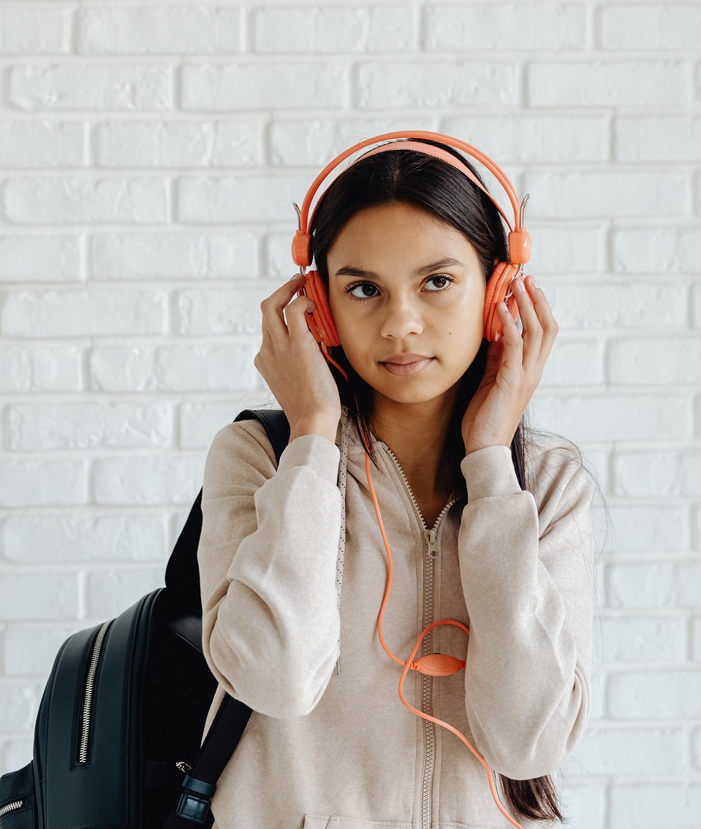 female student with backpack listening to music through headphones