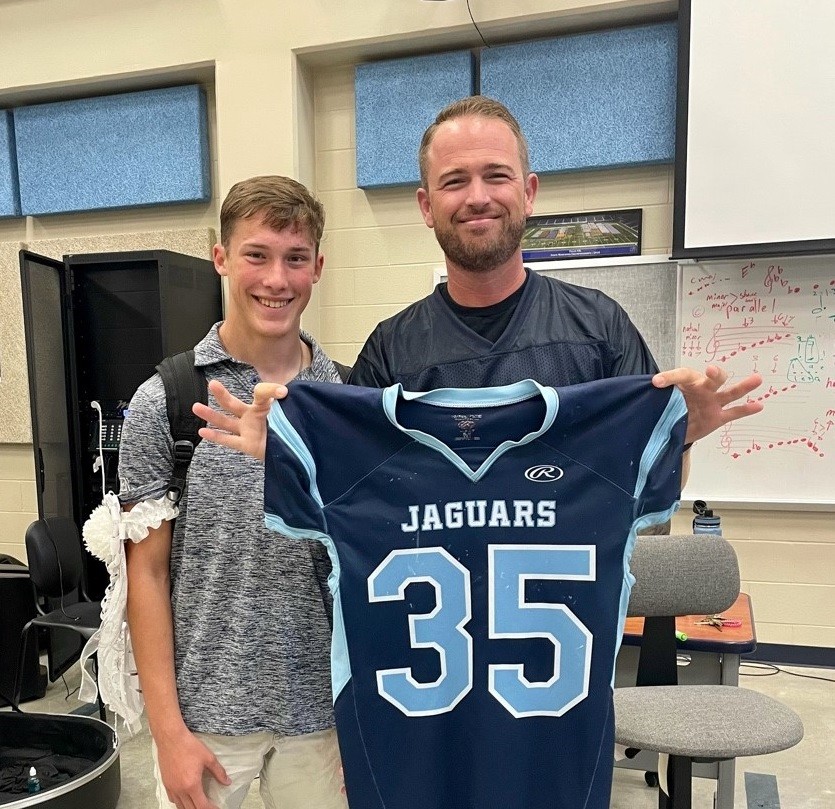 Logan Kitchen, a member of band and football, presents his game-day jersey to band director, Jarrett Lipman 