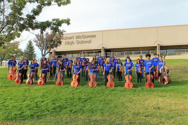 McQueen High School orchestra stands on grass in front of school