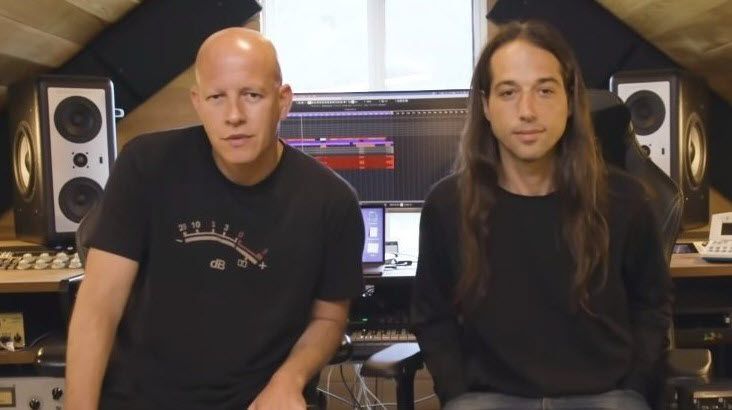 Two men, one bald and one with long hair, sit in front of a digital audio studio setup.