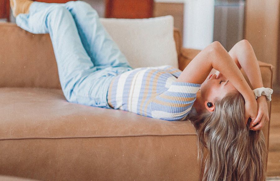 Young woman sprawled on couch wearing earbuds.