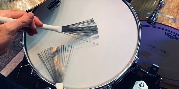 Closeup of someone playing a snare drum with brushes.