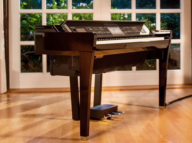 Electronic baby grand piano in the center of an upscale living room with hardwood floors, french doors in the background.