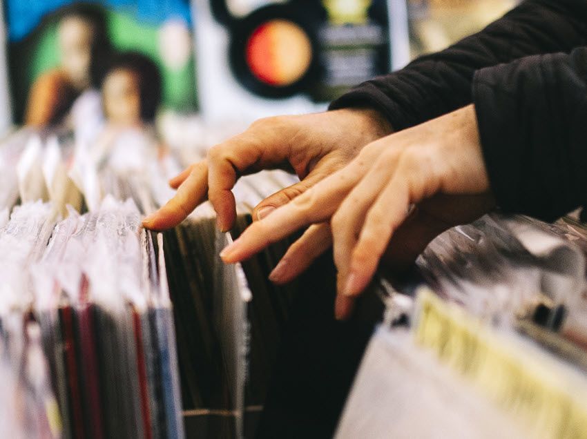 Closeup of someone's hands as they dig through record stacks in a store.