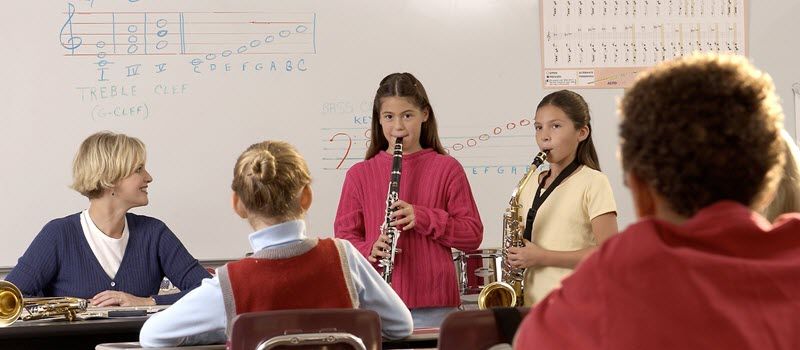 Young students playing woodwinds with a teacher coaching.