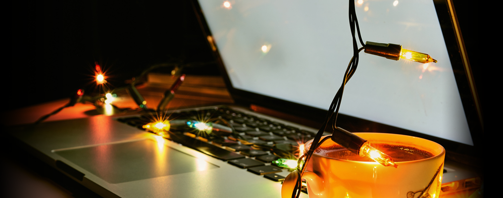 Open laptop with nearby votive candles and strung with holiday lights.