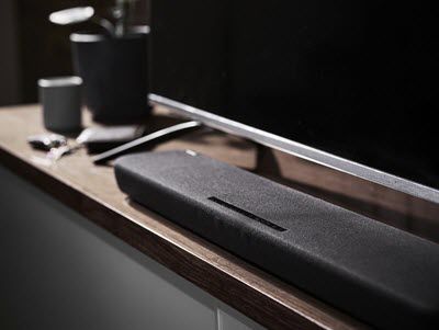 Long slim speaker on counter in front of a flat screen TV.