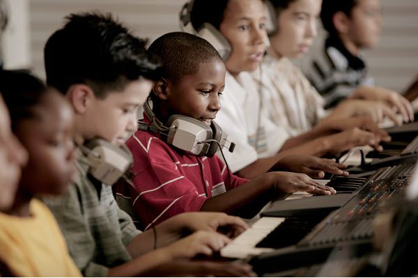 Row of children playing keyboards with headsets around necks.
