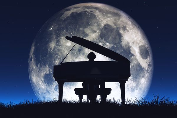 Silhouette of a man playing piano with the moon behind him.