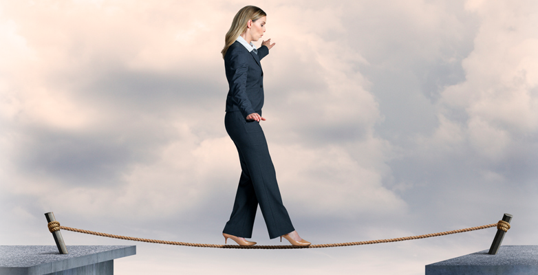 Woman in business suit and high heels walking a tightrope between two buildings.