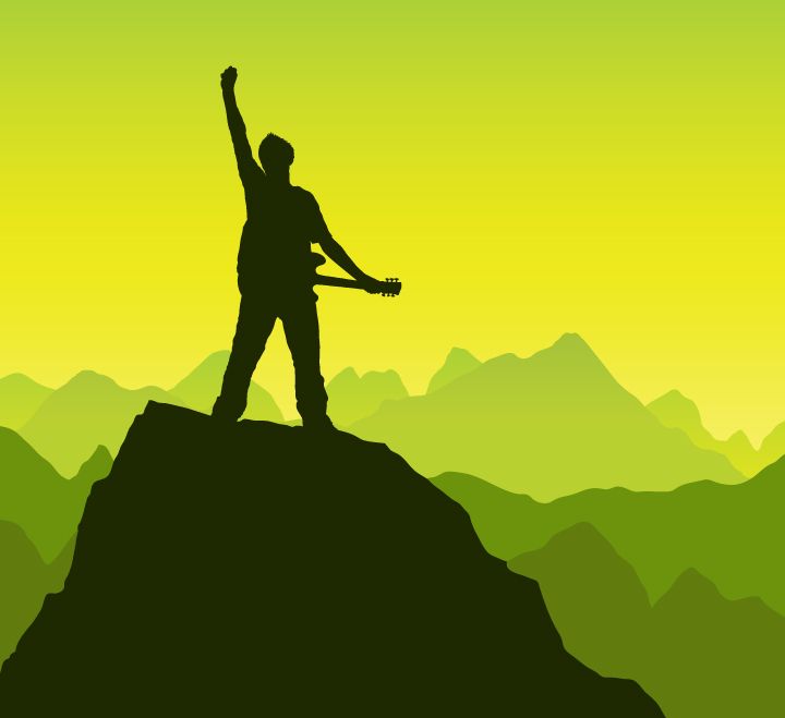 Person in silhouette on top of a mountain peak with an electric guitar and raising fist to the sky.