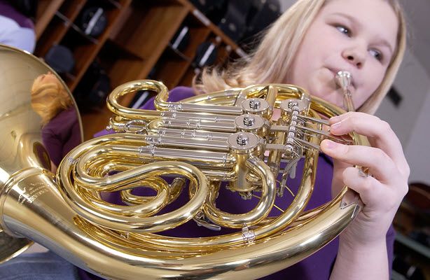 Closeup of French horn being played by a young blonde woman.