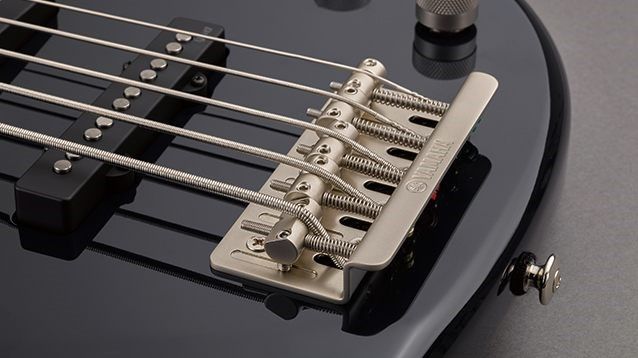 Closeup view of an electric bass' strings stretched over the saddle and the screw at the bottom of the instrument body for adjusting.
