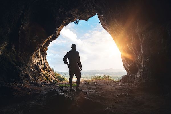View of the silhouette of a person coming out of a dark cave into the bright sunlight.