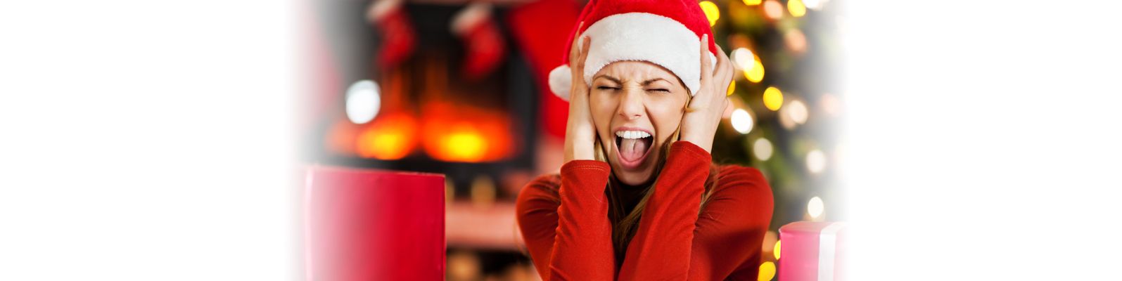 Image of woman screaming while wearing a santa hat in front of a Christmas tree.