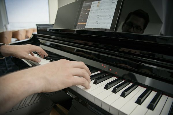 Man playing CSP Clavinova piano along with Scarborough Fair with help of Smart Pianist app displaying the accompaniment sheet music and lights above the keys queuing the pianist to the current and upcoming notes to play.
