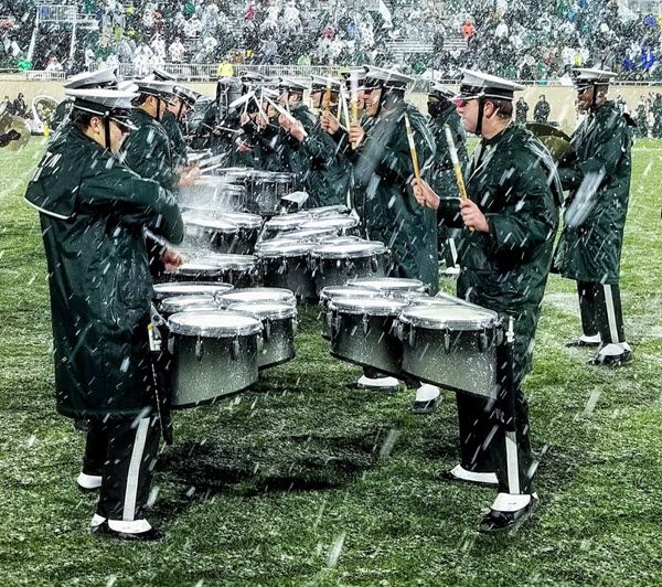 Marching band's drumline lined up playing drums on field while it is raining heavily.