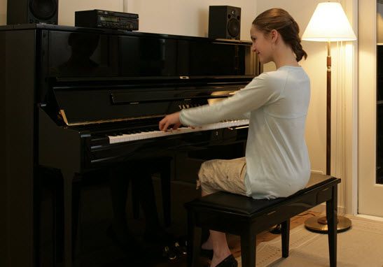 A young girl smiling while playing an upright piano in a living room setting.