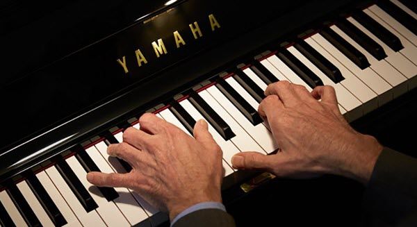Man's hands on a Yamaha piano keyboard.