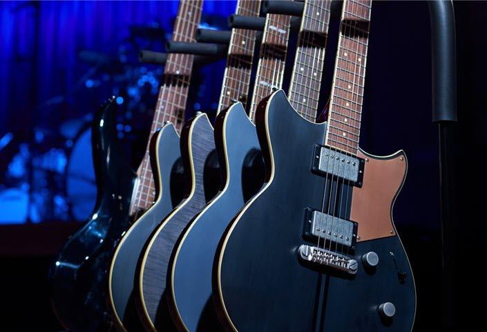Row of electric guitars in their stand on a darkened stage.