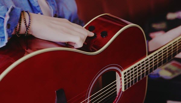 Hands holding a guitar and pressing buttons on side of guitar body.