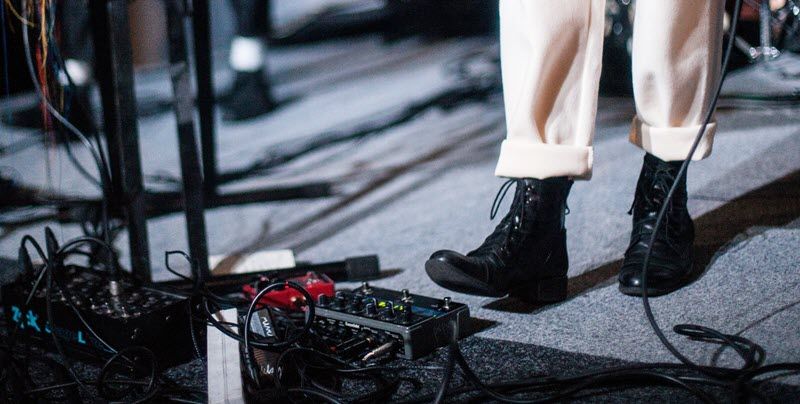 Shot of someone's lower legs in twills and boots using the effects pedals for guitar.