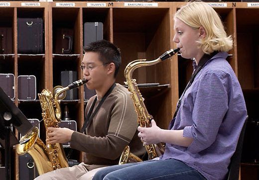 Four young musicians practicing their saxophones in a band room.
