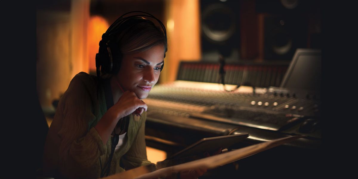 A woman in a darkened recording studio listening through headphones.