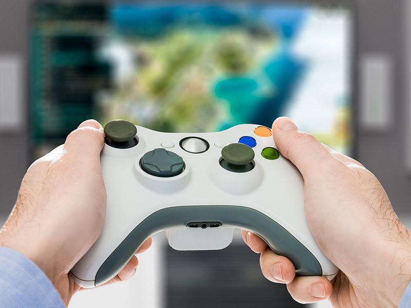 View of a guy's hands using a video game console with video game on screen in background.