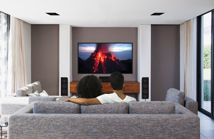A couple cuddling on couch watching a volcano erupt in a movie on the large flat screen.