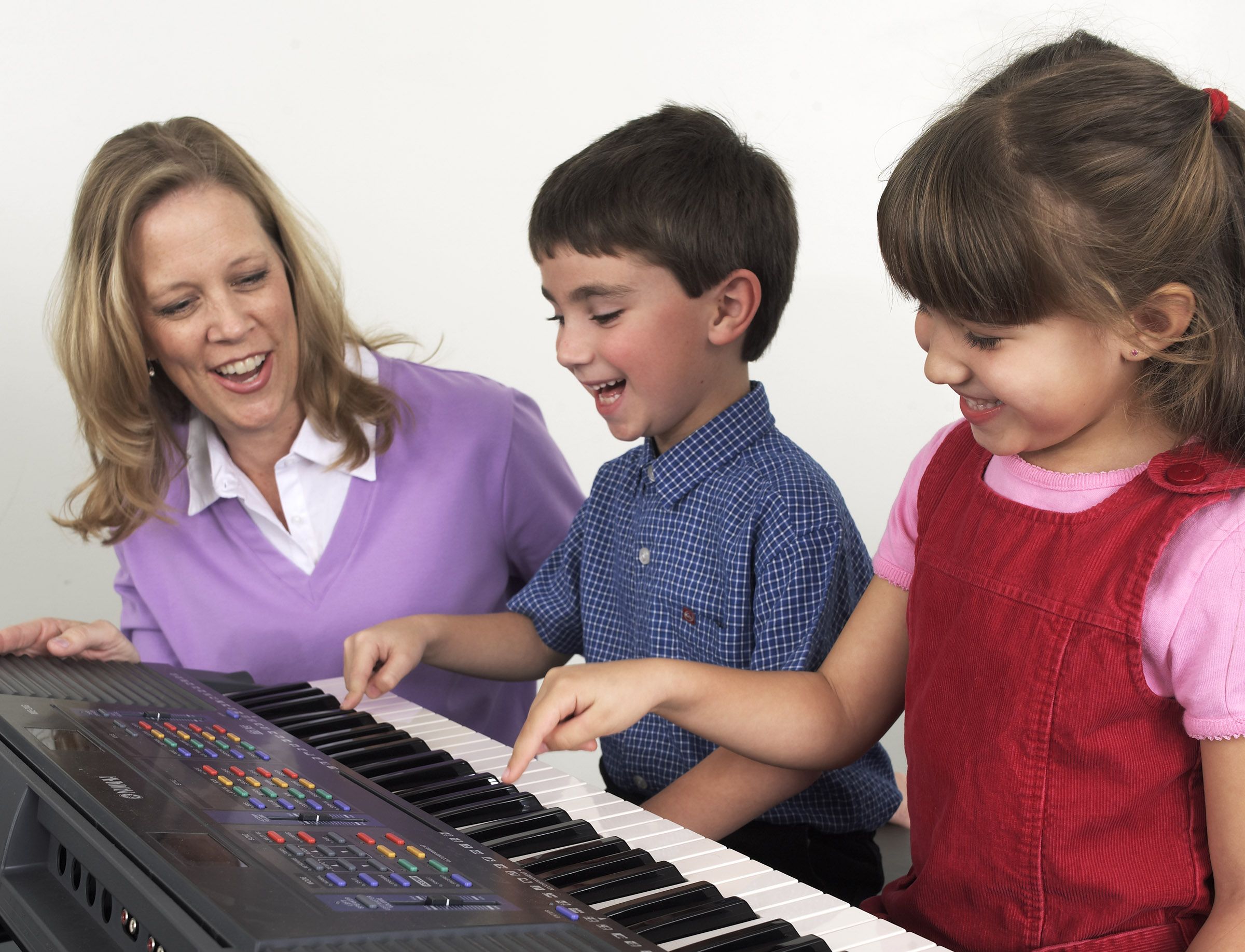 Woman watches as two young children play the keyboard.