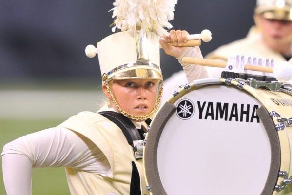Young woman in marching band uniform playing bass drum.