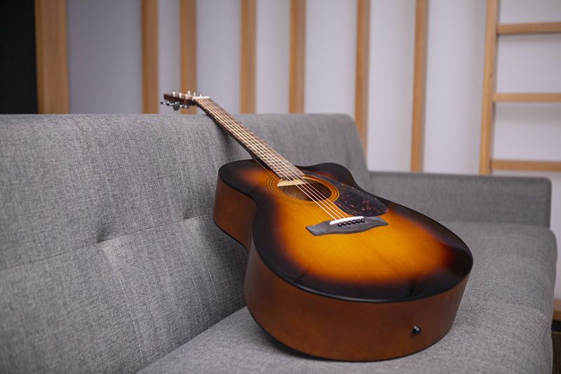An acoustic guitar leaning on a couch.