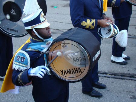 College band member in full uniform marching in parade playing a Yamaha bass drum.