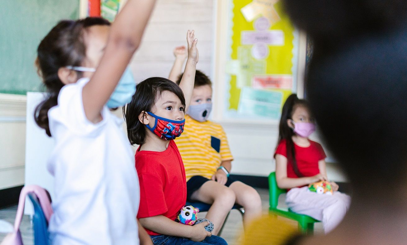 elementary school students raising hands and wearing masks