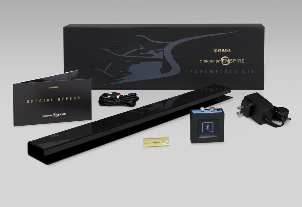A closed box with "Yamaha Disklavier Enspire Essentials Kit" emblazoned on it, plus a variety of small elements placed around the box, including adapters and power source.