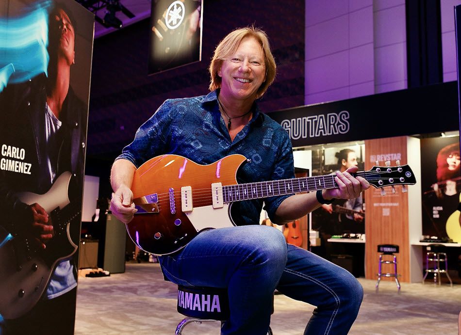 Robbie Calvo playing a Revstar guitar at the NAMM 2022 show from the Yamaha section of the tradeshow floor. Logo is visible, as well as various instruments.