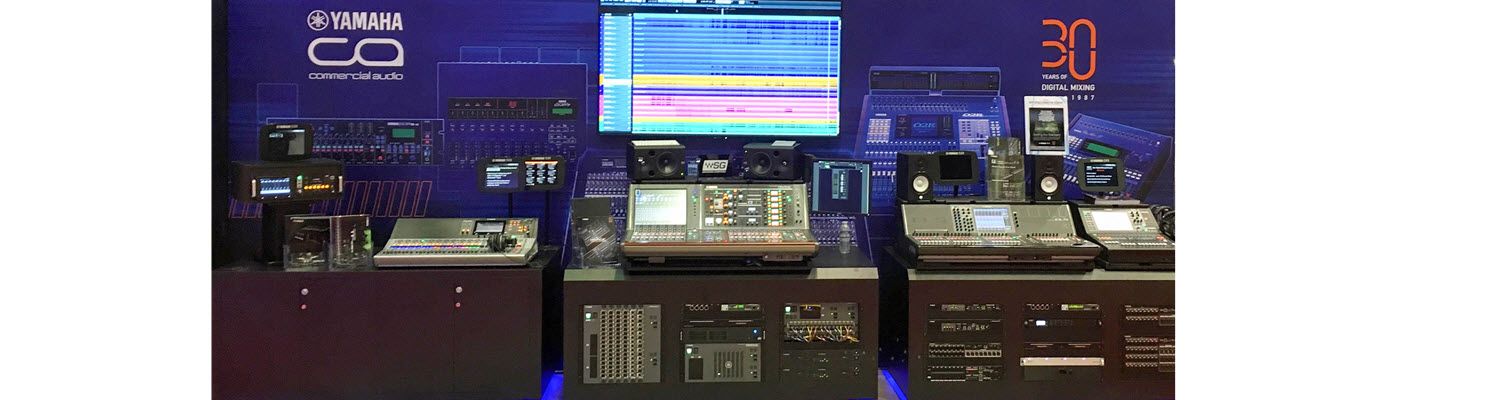 Sound recording equipment with a large computer screen set up for a tradeshow display with Yamaha logo and headlines on the backdrop.