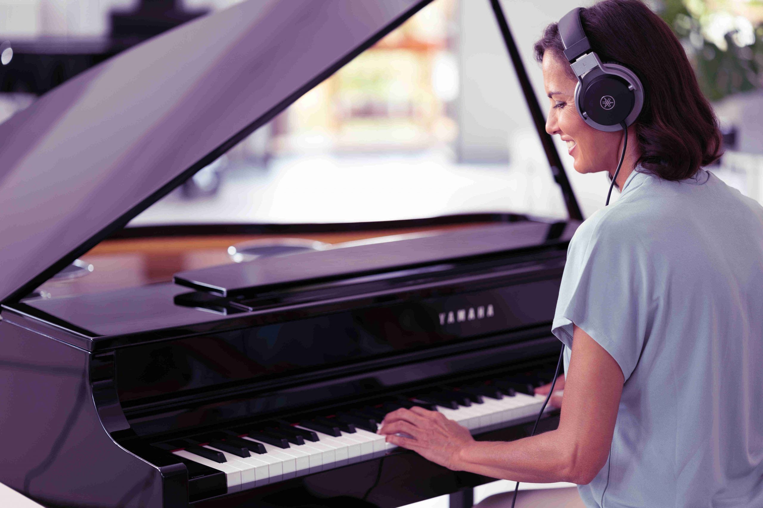 Woman playing grand piano wearing headphones.