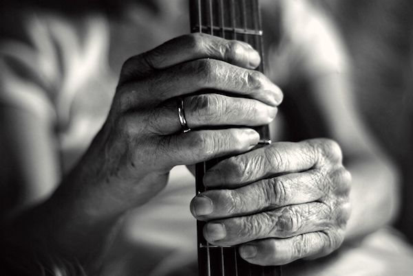 Black and white photograph of woman's hands holding neck of guitar.