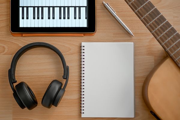 Headphones, guitar, notebook, electronic tablet and pen on wooden background.